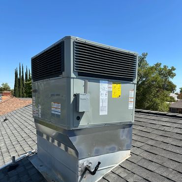 A rooftop HVAC unit installed on a shingled roof under a clear blue sky.