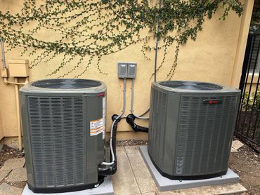 Two outdoor HVAC units installed beside a building with electrical connections.