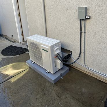Outdoor air conditioning unit installed on a concrete base beside a house wall.