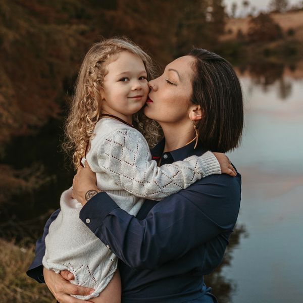 Mother lovingly kisses her daughter by a lakeside.