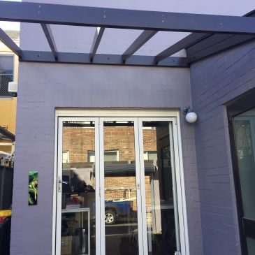 Modern glass door entrance with a gray pergola above.