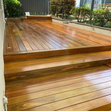 Freshly polished wooden deck with steps in a backyard garden.
