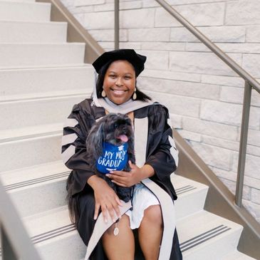 Graduate holding dog on steps.