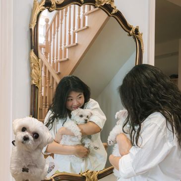 Girl cuddling a small white dog in front of a mirror.