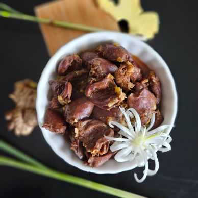 Bowl of cooked chicken gizzards garnished with a white flower on a black surface.