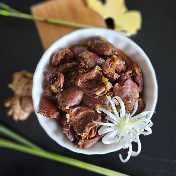 A bowl of cooked chicken hearts garnished with a white flower on a dark surface.