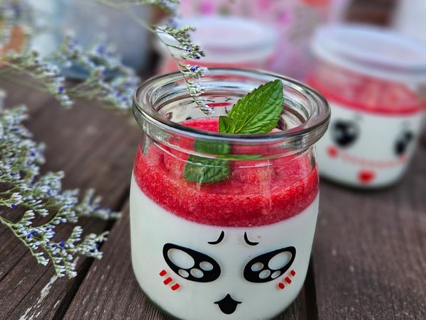 A cute jar dessert with a red topping and mint garnish on a wooden surface.