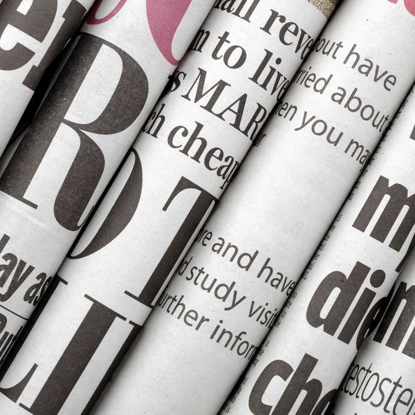 Close-up of folded newspapers showing various text and headlines.
