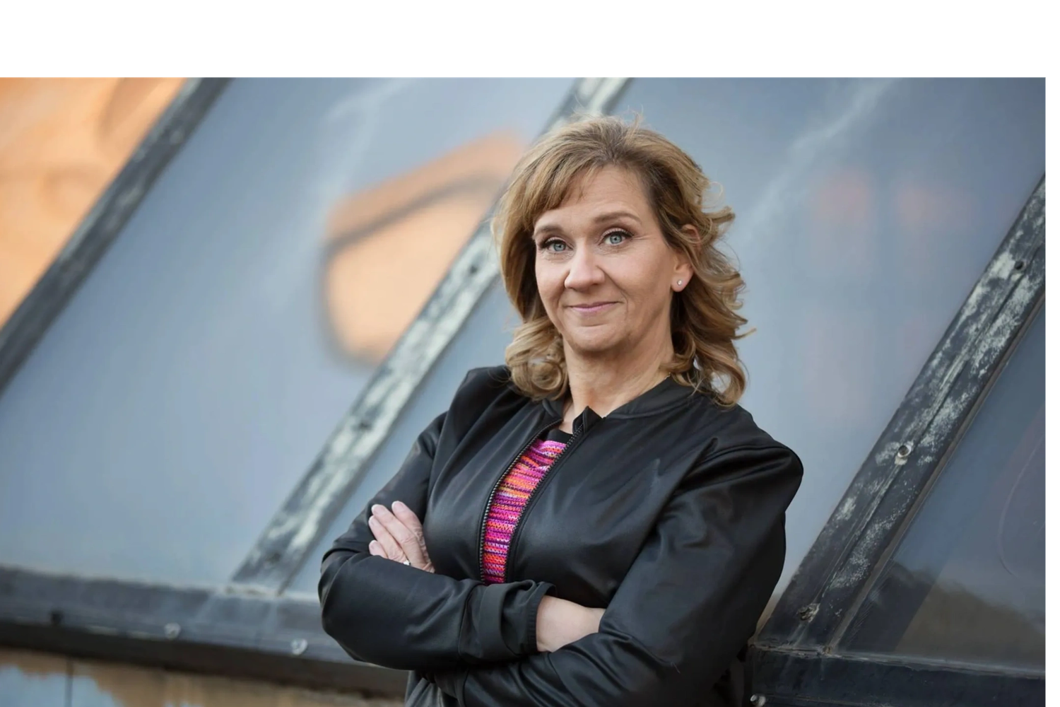 Confident woman with arms crossed, smiling slightly against a modern glass background.