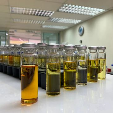 Row of small glass vials filled with various yellowish liquids on a white table.