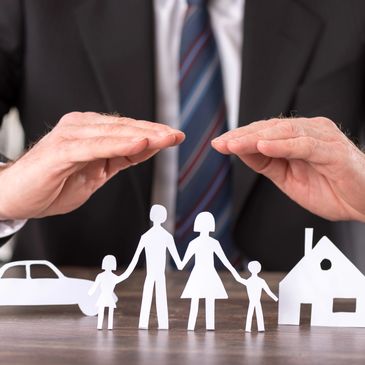 Hands protecting paper cutouts of family, house, and car symbolizing insurance.