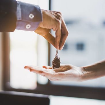 Hand passing a small house keychain to another hand.
