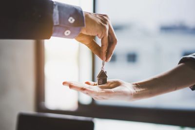 A person handing over a small house keychain to another person.