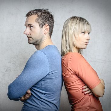 Man and woman standing back to back, arms crossed, looking away.