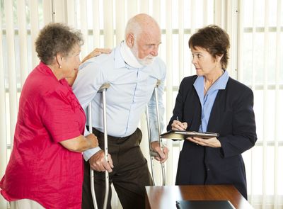 An elderly man with a neck brace and crutches is assisted by a woman while speaking to a professional.