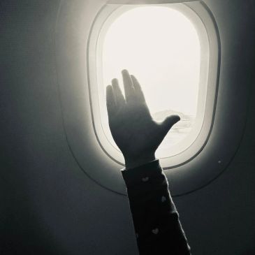 Hand silhouetted against bright airplane window light.