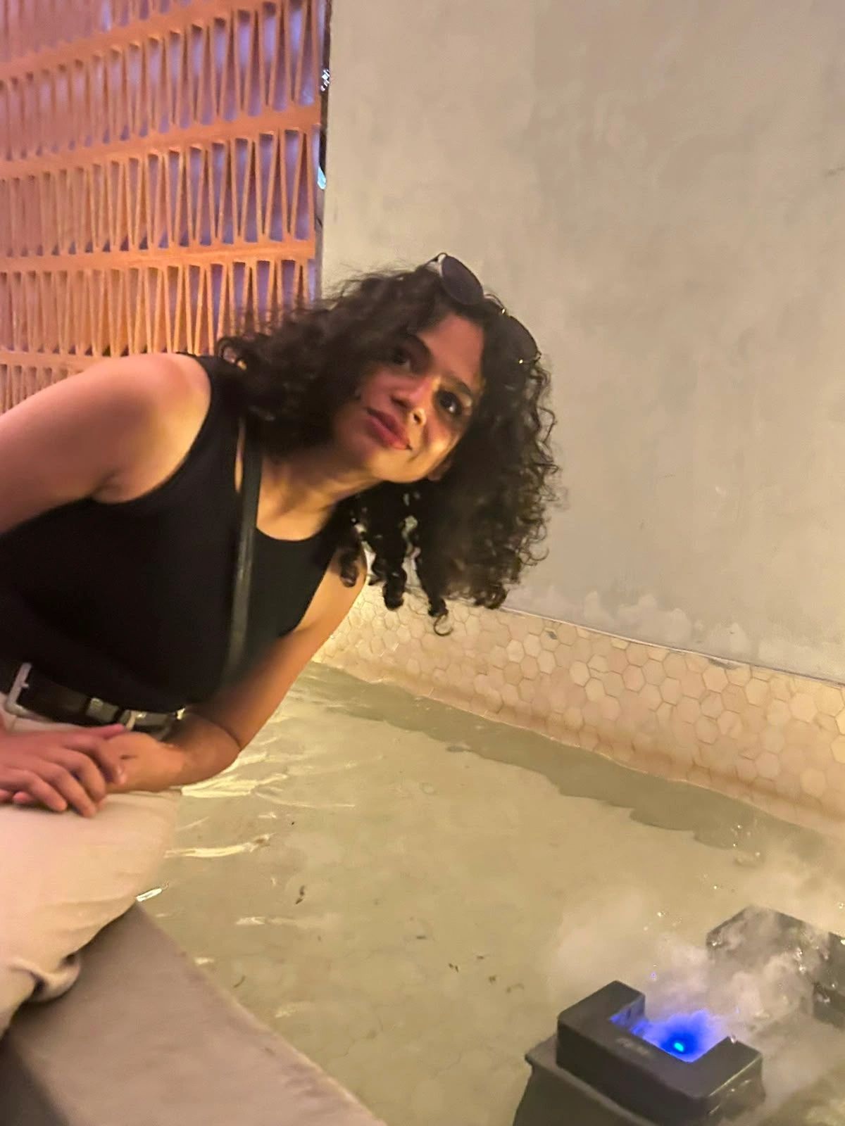 A woman with curly hair smiling near a water feature.