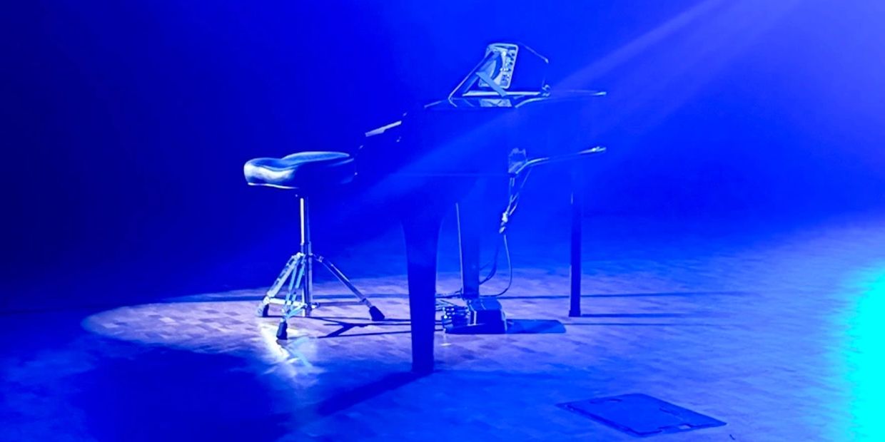 A grand piano and stool illuminated by blue stage lights.