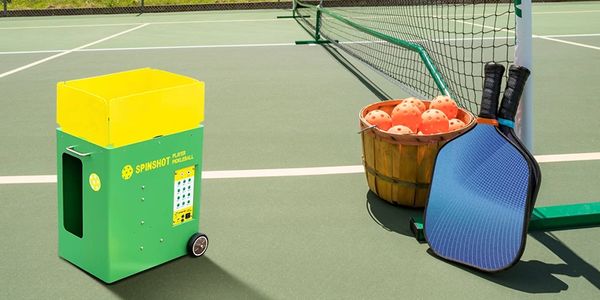 Spinshot pickleball machine, pickleball paddles and balls on a courts ready to be used