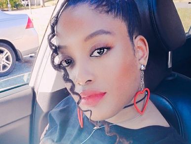 Black woman in a car with red lipstick, red heart earrings.