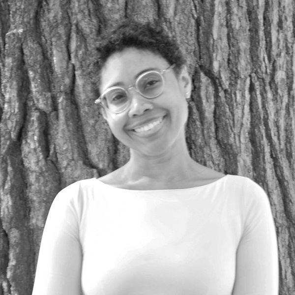 Smiling woman with glasses standing in front of a tree.