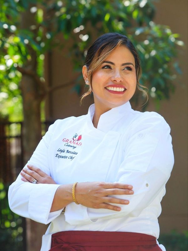 Smiling female chef in white coat outdoors.