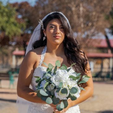 Bride holding a bouquet of white flowers outdoors.