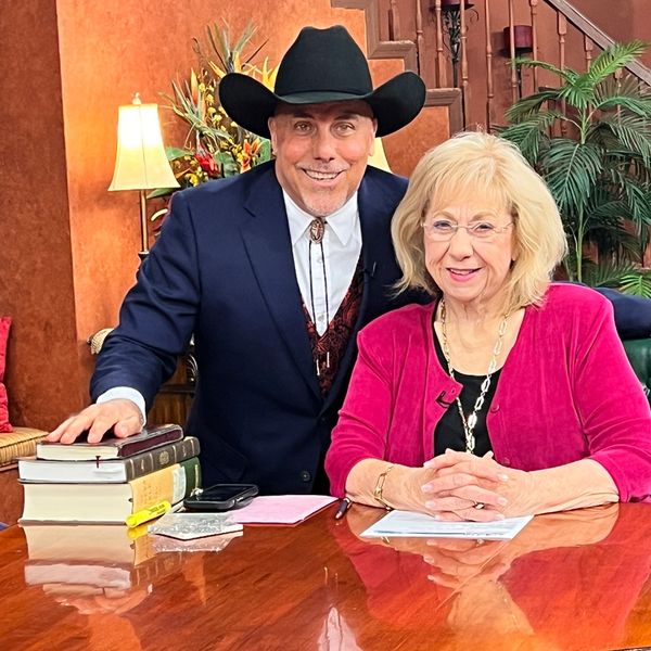Two people smiling at a table with books and papers in a warmly decorated room.