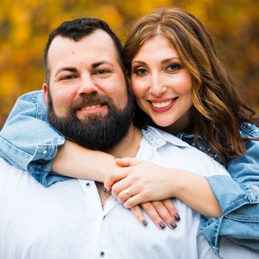 Happy couple embracing outdoors with autumn foliage in the background.