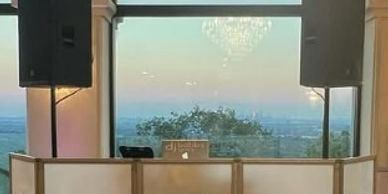 DJ setup with large speakers in front of a scenic window view.