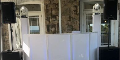 A DJ booth setup with speakers and lighting in front of a stone wall indoors.