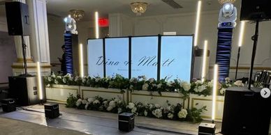 Elegant wedding stage setup with floral decorations and LED screens.