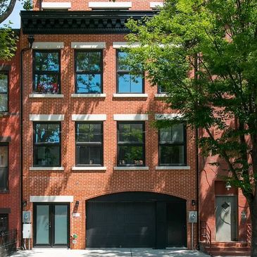Modern brick townhouse with black garage door and trees.