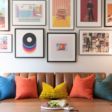 Colorful pillows and framed art above a brown couch.