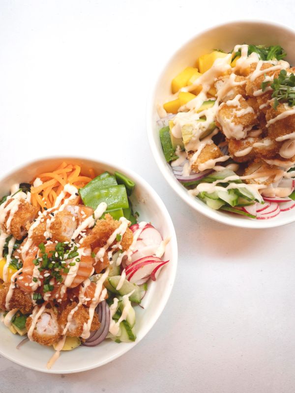 Two colorful poke bowls with fresh ingredients and drizzled sauce.