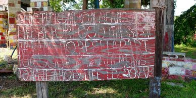 Old wooden sign with faded white text in a grassy area.