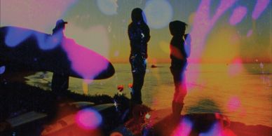 Silhouetted figures near water at sunset with colorful light effects.