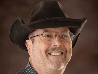 Smiling man wearing glasses and a cowboy hat.
