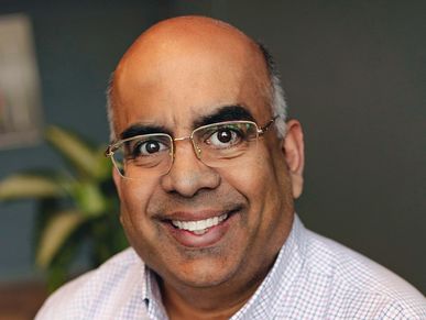 Smiling man with glasses and a checkered shirt.