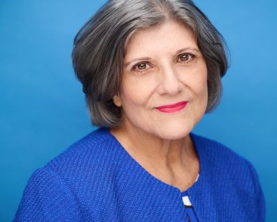 Confident older woman smiling against a blue background.