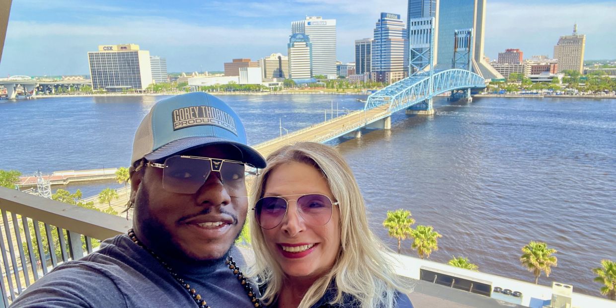 Couple smiling with city skyline and river bridge in the background.
