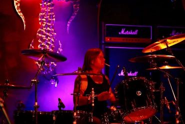 A drummer playing on stage with vibrant purple lighting and Marshall amplifiers.