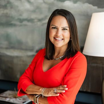 Confident woman in red dress smiling with arms crossed indoors.