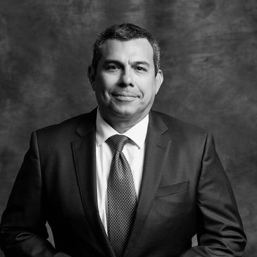 Confident man in a navy suit with a red tie against a dark backdrop.