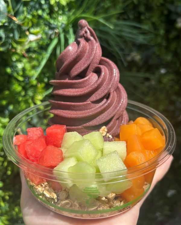 A colorful acai bowl topped with fresh fruit and granola in a clear cup.