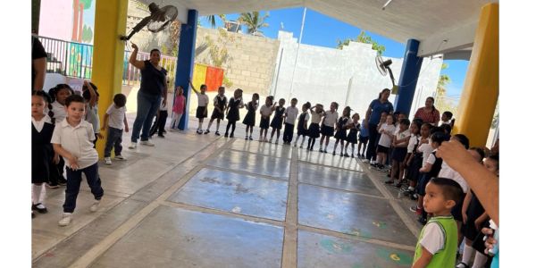 Children and adults standing in a semi-circle in a covered outdoor area.