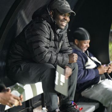 Three men sitting and smiling on a bench, two using phones.