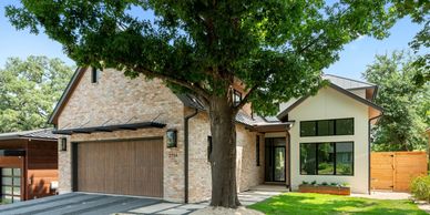 Modern house with stone facade and large tree in front.