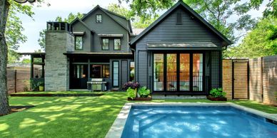 Modern dark gray house with large windows and a backyard pool.