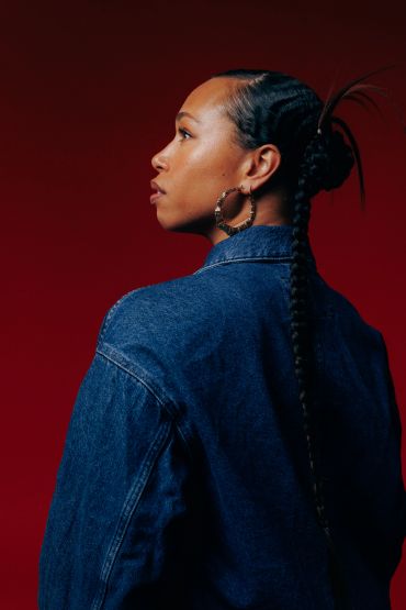 Profile of woman in denim jacket with red background.
